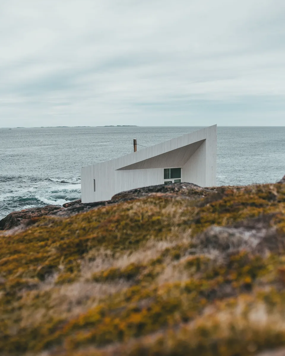 A white timber studio, all angles, alone on a headland above a grey sea